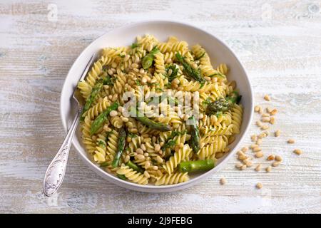 Pasta vegana con asparagi, aglio, pinoli e prezzemolo su sfondo ligneo. Semplice cibo fatto in casa Foto Stock