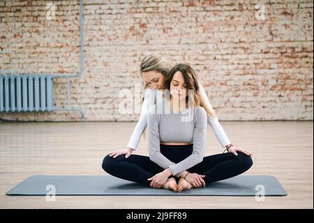 L'istruttore di yoga aiuta la donna incinta a distendere gambe e muscoli in una lezione di yoga seduta sul tappeto Foto Stock