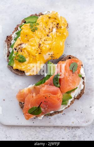 Uova strapazzate con salmone affumicato, formaggio spalmabile e avocado su pane tostato Foto Stock