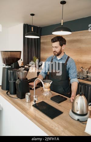 Il bel barista macina i chicchi di caffè in coffee emachine Foto Stock