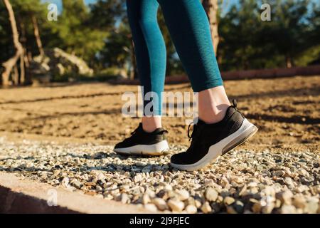 Giovane donna che indossa pantaloni blu e scarpe nere camminando e correndo su sfondo verde natura. Concetto di salute, esercizio fisico e allenamento cardio all'aperto. Foto Stock