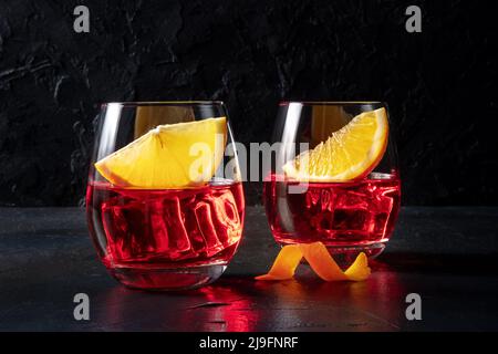 Aperitivo Campari con fette d'arancia fresche, su sfondo nero. Una bevanda alcolica, un cocktail estivo, due bicchieri Foto Stock
