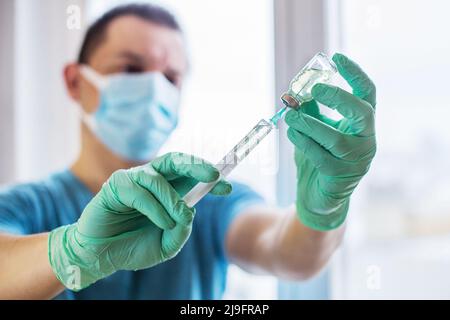 Mani del medico che riempie una siringa. L'uomo ha le mani in guanti blu che tengono il vaccino. Medicinale, vaccinazione e concetto di farmaco Foto Stock