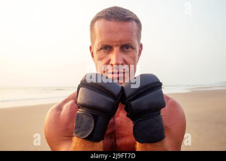 Forte pugile uomo che fa durante l'esercizio di kickboxing lotta con l'allenatore al tramonto .close ritratto di bello fitness maschio modello bodybuilder rabbia, rabbia Foto Stock