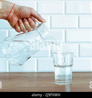 Una mano dell'uomo che versa l'acqua pura fresca dalla bottiglia in un bicchiere sul tavolo, concetto di salute e dieta Foto Stock