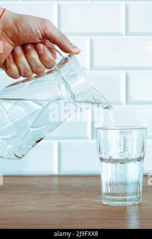 Una mano dell'uomo che versa l'acqua pura fresca dalla bottiglia in un bicchiere sul tavolo, concetto di salute e dieta Foto Stock