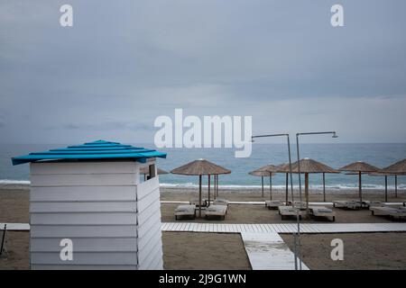 Scena estiva con ombrelloni di canna, sdraio e cabine spogliatoi in spiaggia Foto Stock