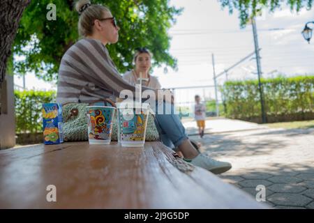 Due donne che scherzavano il loro caffè del mattino seduto su una panchina al parco Foto Stock