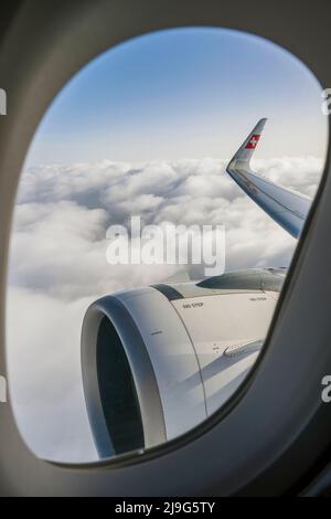 Vista della finestra dell'ala destra e del motore di un Airbus svizzero A320-200 neo che vola sulle nuvole Foto Stock