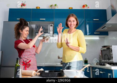 Due donne cucinano felicemente in cucina, gettando la farina l'una all'altra. All'interno. Il concetto di coppie LGBT e divertimento. Foto Stock