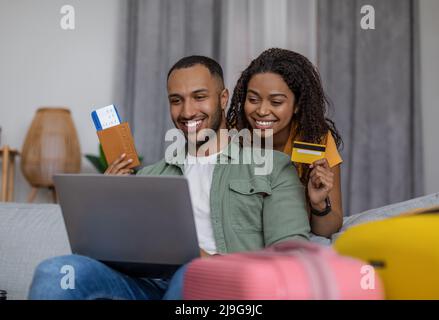 Felice coppia afroamericana usando il portatile e prenotare l'hotel con la carta di credito, seduto con le valigie, pronto per andare Foto Stock