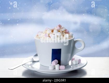 tazza di caffè con marshmallow sul tavolo in caffetteria contro finestra nella notte invernale nevicante Foto Stock