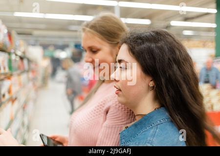 Shopping al negozio di alimentari. Due giovani donne scelgono i prodotti nel negozio. In background, il piano di negoziazione del negozio. Foto Stock