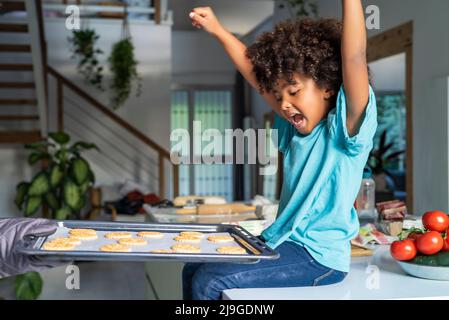 Mano della madre che mostra i biscotti cotti al forno della figlia in cucina Foto Stock