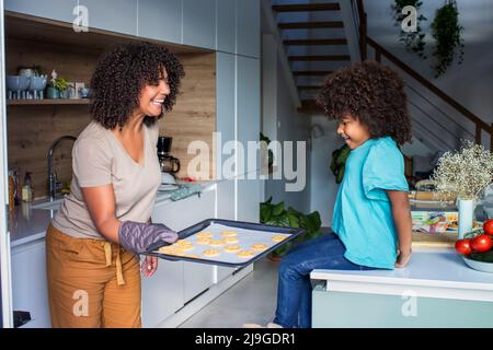 Madre sorridente che mostra la figlia biscotti al forno in cucina Foto Stock