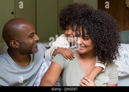 Smiling family sitting together on bed Foto Stock
