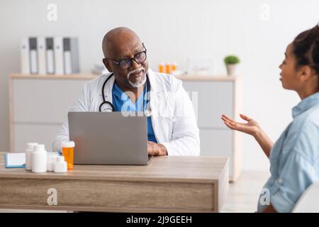 Maturo medico nero che ascolta la giovane paziente femminile Foto Stock