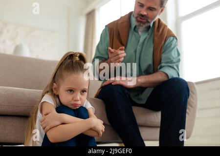 Padre severo che scolding la figlia triste piccola seduta a casa Foto Stock