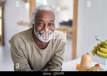 Uomo anziano sorridente appoggiato sul piano di lavoro della cucina Foto Stock