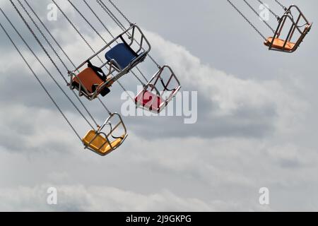 posti a sedere vuoti di colore primario per un giro di divertimento contro il cielo con le nuvole Foto Stock