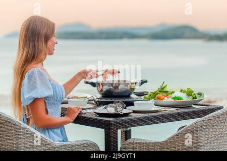 Donna che cucina shabu shabu in hot pot su stufa in ristorante giapponese con mare Foto Stock