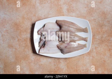 Vista dall'alto di un font bianco con sei pesci macromi su uno sfondo astratto marmorizzato dello studio. Cucina mediterranea. Foto Stock