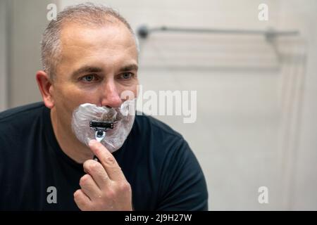 Uomo che rasa con il rasoio utilizzando schiuma in bagno al mattino Foto Stock