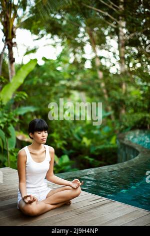 Una giovane donna asiatica medita in una villa con piscina privata a Kayumanis Ubud, Bali, Indonesia. Foto Stock