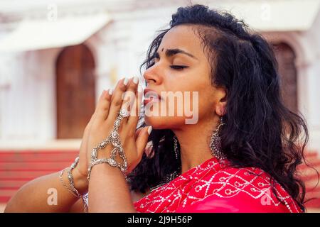 Giovane donna indiana in tradizionale sari rosso vestito pregare in un tempio indù goa india Hinduism.girl esecuzione namaste gesto cattolicesimo Delhi Street Foto Stock