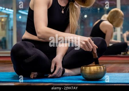 Meditazione della donna con ciotola di canto tibetano durante la pratica dello yoga sul tappeto Foto Stock