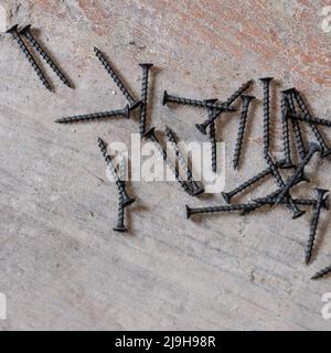 Le viti metalliche nere si trovano sul pavimento in calcestruzzo, le viti sul legno. Foto Stock