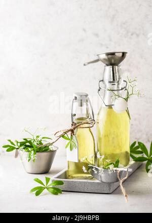 Due bottiglie di vetro di sciroppo di legnoso dolce fatto in casa in un vassoio grigio con foglie verdi fresche. Sano concetto di cibo estivo. Messa a fuoco selettiva. Spazio di copia. Foto Stock