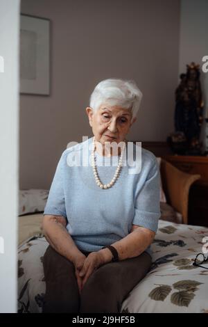 Donna anziana preoccupata seduta a letto a casa Foto Stock
