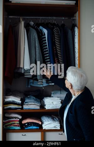 Donna anziana che sceglie i vestiti nell'armadio a casa Foto Stock