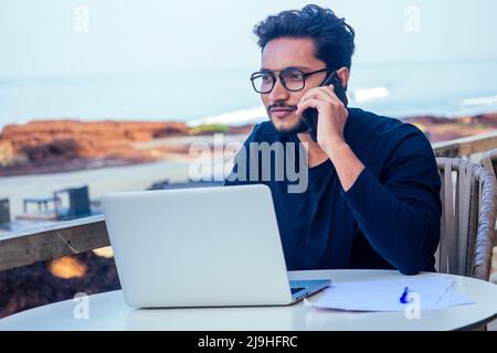 uomo che parla al telefono india estate holidays.stylish giovane uomo indiano freelancer lavorando con laptop freelance surf online.businessman a distanza Foto Stock