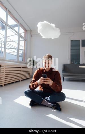 Un uomo d'affari sorridente che utilizza uno smartphone in ufficio sotto una rete cloud sempre più stabile Foto Stock