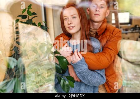 Ragazzo che abbraccia la ragazza da dietro visto attraverso il vetro Foto Stock