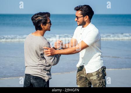 Holi felice due indian elegante mans giovani amici abbracciato sulla spiaggia dal mare.a lungo atteso incontro diwali dei fratelli in India Goa tropicale Foto Stock