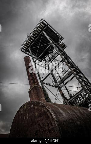 Gennaio 2011: Una drammatica prospettiva a bassa angolazione di una struttura metallica imponente e di un camino adiacente in mattoni presso l'ex ospedale di Fairmile a Cholsey, Oxfordshire. Contro un cielo cupo e coperto, la scena mette in risalto l'architettura industriale imponente e i resti scheletrici duraturi dell'infrastruttura utilitaria della struttura, enfatizzando la bellezza spoglia del suo abbandono. Foto Stock