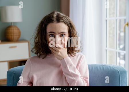 Giovane donna che ricopre la bocca con mano a casa Foto Stock