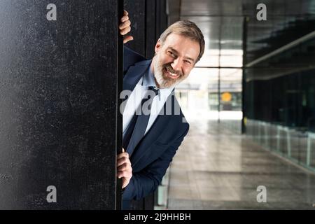 Un uomo d'affari felice che sbirca da dietro la colonna nera Foto Stock