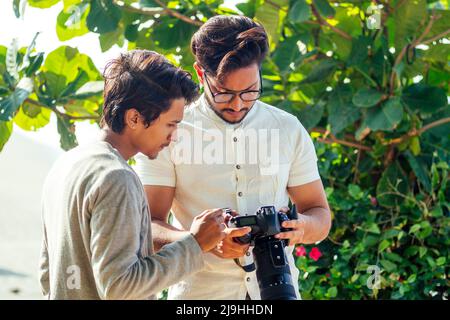 bel fotografo indiano e sicuro con una grande fotocamera professionale che scatta foto scattando foto sulla spiaggia.sessione fotografica in estate Foto Stock