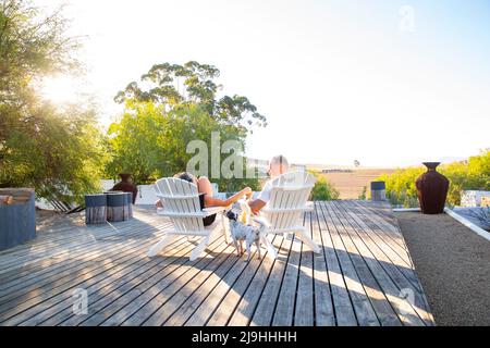 Uomo e donna seduti su una sedia con il cane che si gode il tramonto Foto Stock