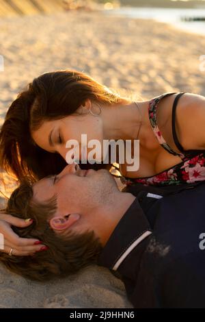 Coppia giovane che si abbraccia l'un l'altro giacendo sulla sabbia alla spiaggia Foto Stock