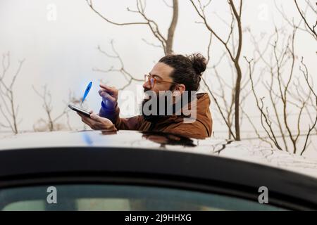 Uomo sorridente che tocca l'icona di navigazione sullo smartphone in auto Foto Stock