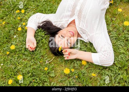 Donna felice con fiore giallo che giace sull'erba al parco Foto Stock