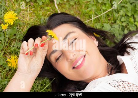 Donna felice con fiore giallo giacente sull'erba Foto Stock