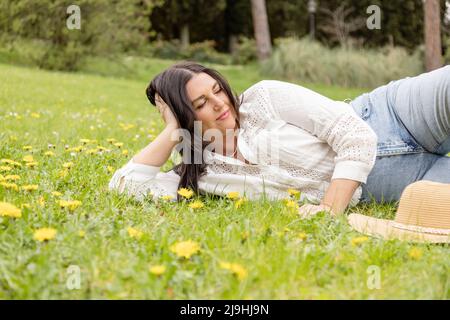 Donna sorridente sdraiata sull'erba al parco Foto Stock