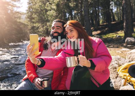 Giovane donna che prende selfie con uomo bearded attraverso il telefono intelligente in giorno di sole Foto Stock