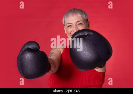 Donna felice che indossa guanti da boxe in piedi su sfondo rosso Foto Stock